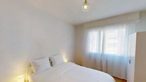 A bedroom with a bed, bedside lamps, a window with sheer curtains, and a wardrobe.