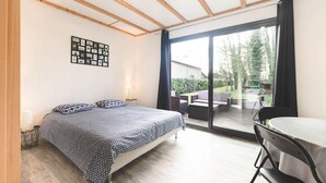 Ein Schlafzimmer mit einem Bett, einer Wandcollage aus Fotos und einer Glasschiebetür zu einer Terrasse mit Gartenmöbeln.