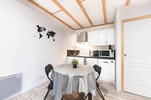 A compact kitchen with white cabinets, a microwave, and a small dining area with a round table and chairs. - Le Gite du Prunus - MONTAMISE (MONTAMISE)