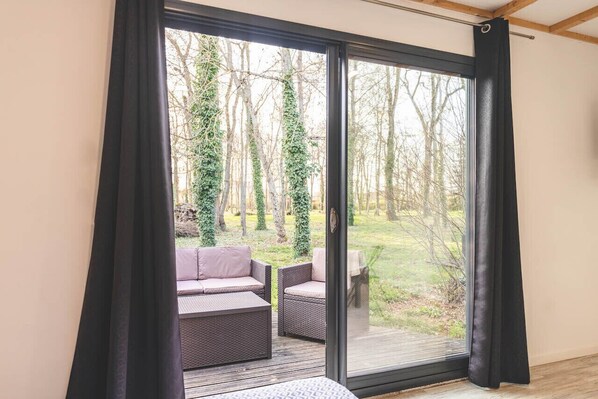 A room with a sliding glass door leading to an outdoor deck with wicker furniture and a view of trees. - Le Gite du Prunus - MONTAMISE (MONTAMISE)