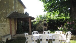 Zona d'esmorzar a l'aire lliure rústica, amb un edifici de pedra, una pérgola de fusta i un forn de rajola.