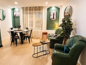 Un salon comprenant une table à manger, des chaises, un canapé vert, une petite table basse et une plante en pot.