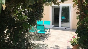 En terrasse med et bord, stole, en skydedør og en potteplante.