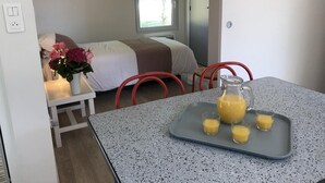 Une chambre d’hôtel compacte, avec un lit, une petite table sur laquelle se trouve un plateau avec du jus d’orange, et une fenêtre donnant sur un paysage verdoyant.