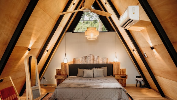 Un dormitorio estilo loft con techo de madera, cama con cabecera de madera y una lámpara colgante.