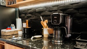 Una cocina con cafetera, utensilios y pared de ladrillo.