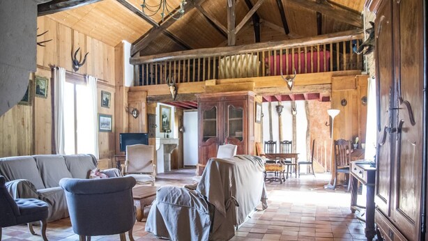 A spacious room with wooden walls, a high ceiling, and a chandelier. There are several pieces of furniture including a sofa, chairs, and a table. - Le Verger - ANCHE - Gîte (ANCHE)