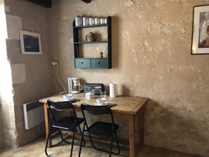 Ein kleiner Essbereich mit einem Holztisch, zwei schwarzen Stühlen, einer Kaffeemaschine und einem Regal mit Küchenutensilien.