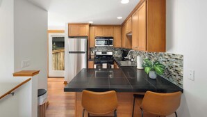 A modern kitchen with wooden cabinets, a black countertop, and two bar stools. - Modern City Retreat • Family Friendly • Free Prkg (Seattle)