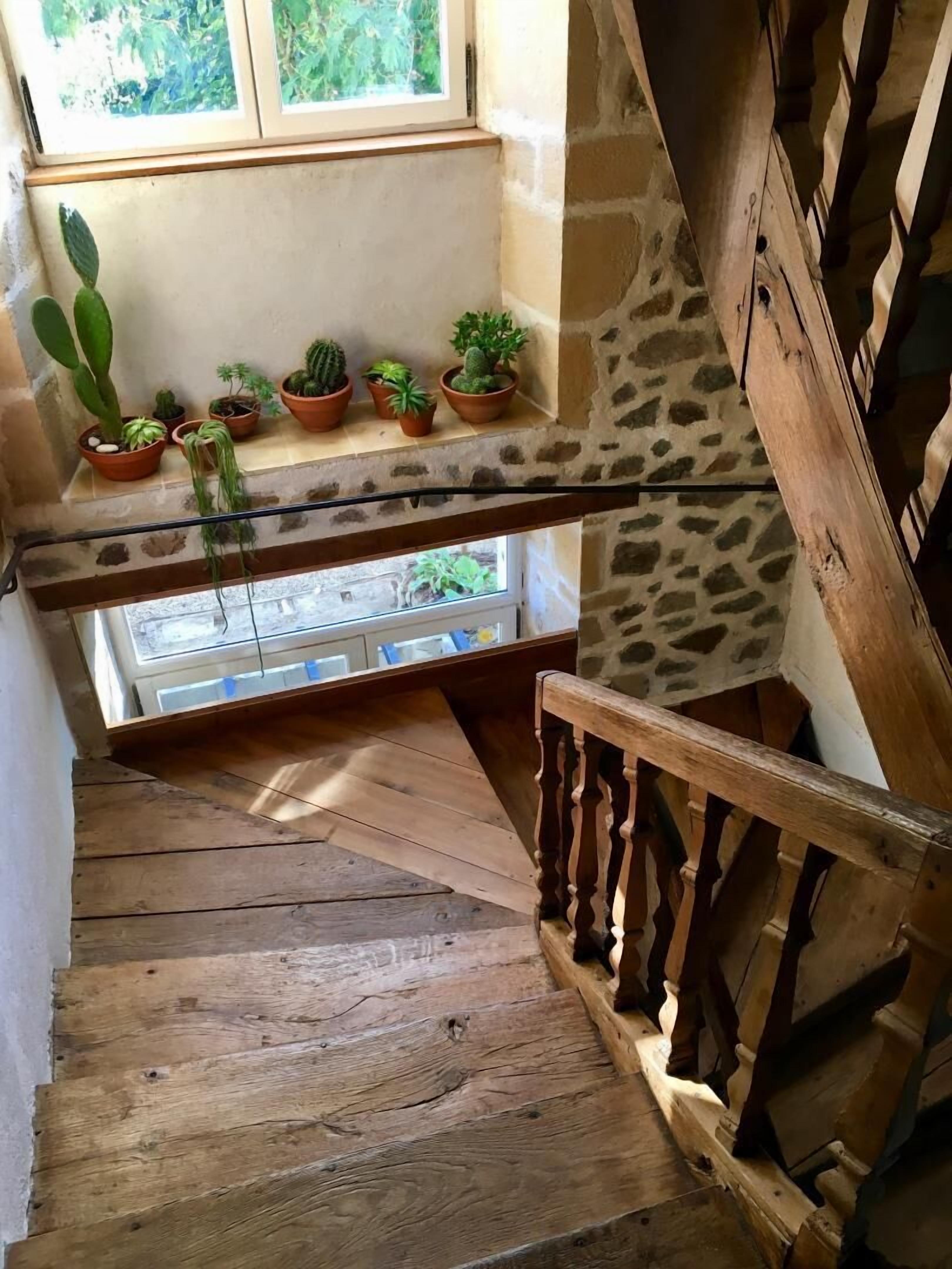 Un escalier en bois avec une rampe, un mur en pierre et une fenêtre ornée de pots de plantes sur le rebord.