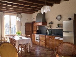 A kitchen with wooden cabinets, a dining table, chairs, a refrigerator, and a clock on the wall. - The House of Villars (PRESSAC)