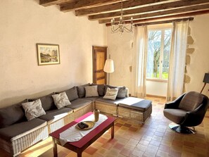 Una sala de estar con un sofá modular, una butaca, una mesa y un ventanal con cortinas.
