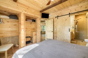 Ein Holzblockhaus-Innenraum mit einem Bett, einem Sessel, einem Fernseher und einer Schiebetür zu einem Badezimmer.