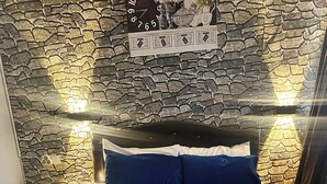 A bed with blue and white bedding, a wooden headboard, and a stone wall with a clock.