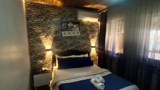 A bedroom with a stone wall, a bed with a blue bedspread, a clock, and a nightstand.