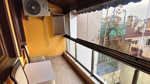 A balcony with a wooden ceiling, a ceiling fan, a window with a view of buildings, and a table with chairs.