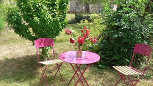 Un jardín con una mesa y sillas, rodeado de follaje y flores.