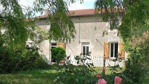 Un edificio de piedra con jardín, cerca y rosal.