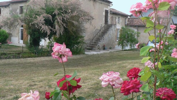 Un rústico edificio de piedra con tejado de tejas, una escalera y un jardín de rosas.