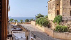 A view from a balcony overlooking a coastal road with a historic stone building and a clear view of the sea.