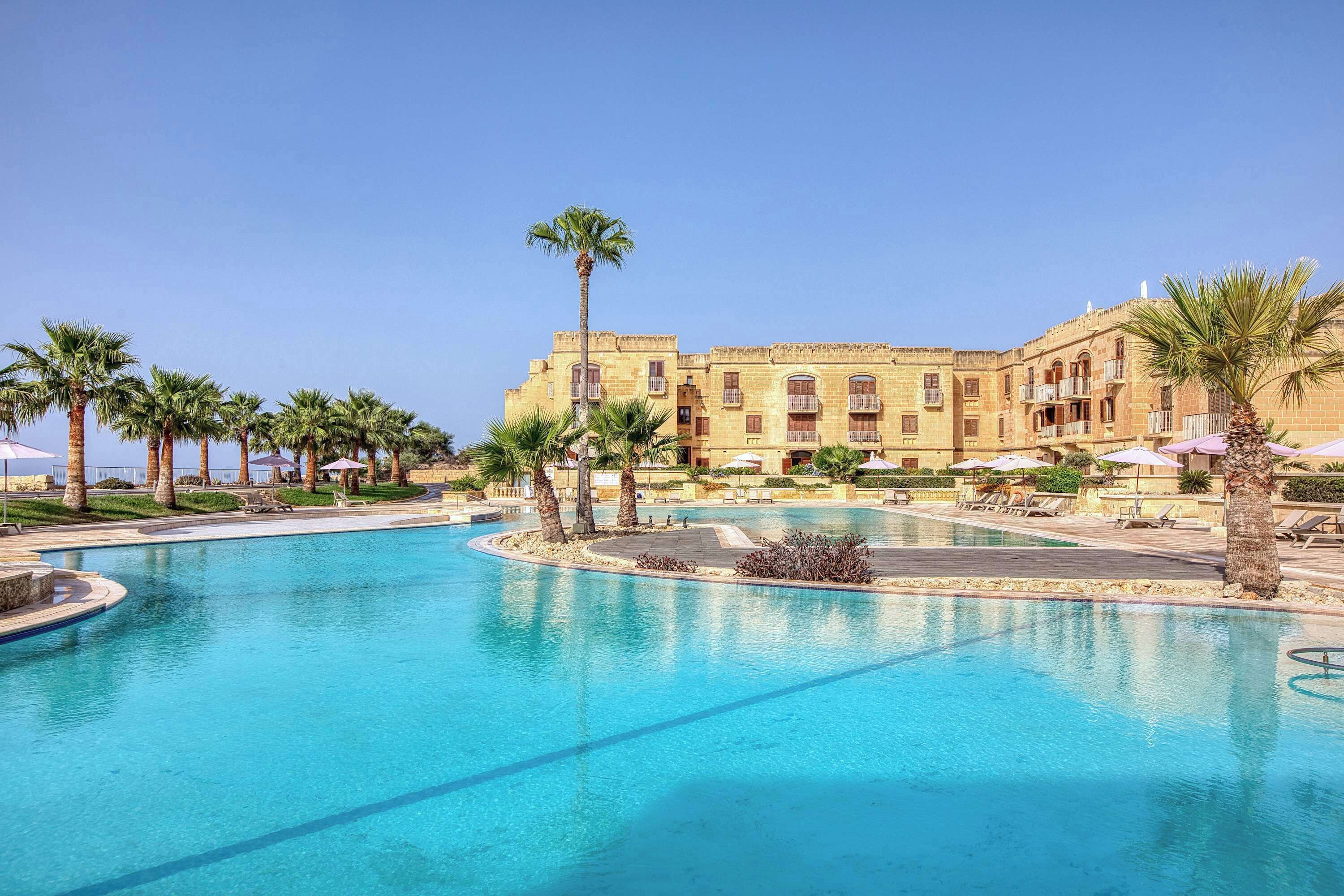 A resort with a large swimming pool, palm trees, and a building with multiple balconies.