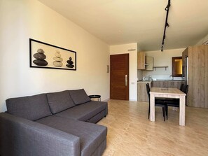 A living room with a sofa, a dining table with chairs, a kitchen area, and a door.