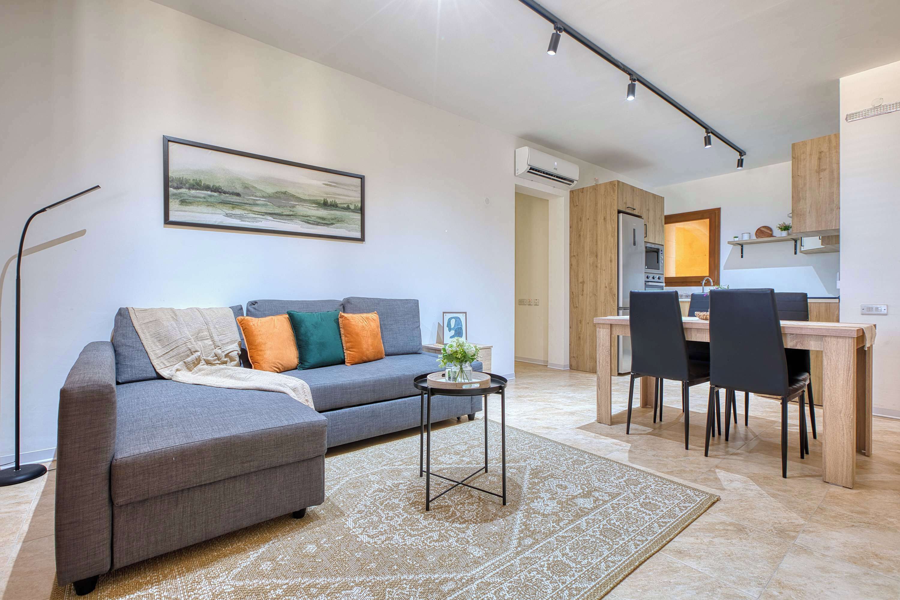 A modern living room with a grey sofa, a small side table, and a dining area with a wooden table and chairs.