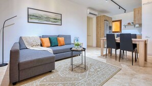 A modern living room with a grey sofa, a small side table, and a dining area with a wooden table and chairs.