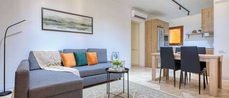 A modern living room with a grey sofa, a small side table, and a dining area with a wooden table and chairs.