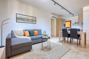 A modern living room with a grey sofa, a small side table, and a dining area with a wooden table and chairs.