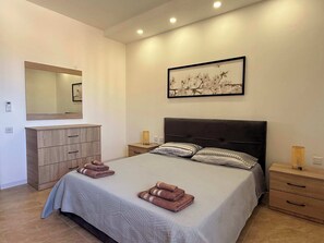 A bedroom with a bed, a dresser, a nightstand, a lamp, and a framed picture on the wall.