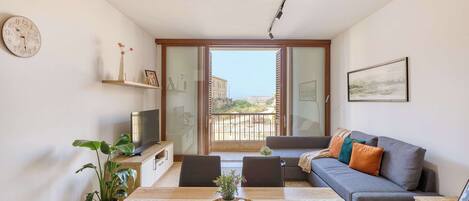 Un salón moderno con una mesa de comedor, sofá, televisor y un balcón con vistas.