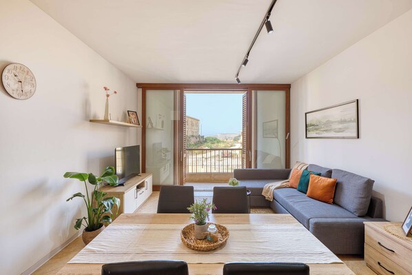 A modern living room with a dining table, sofa, TV, and a balcony with a view.