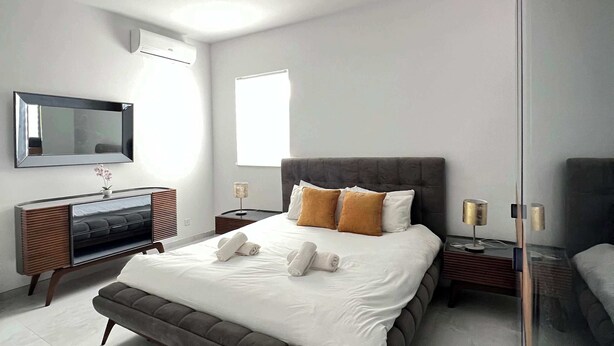 Un dormitorio moderno con una cama grande, una mesita de noche, un espejo y un aire acondicionado de pared.