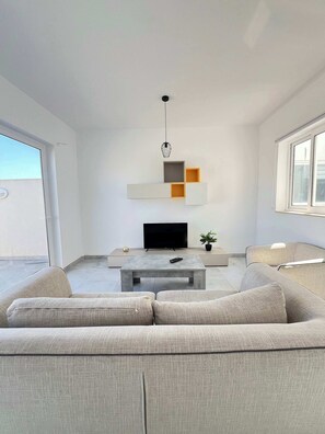 Ein modernes Wohnzimmer mit einer Couch, einem Couchtisch, einem Fernseher und minimalistischer Wandgestaltung.