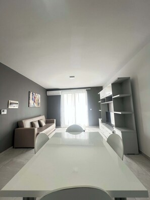 A modern living room with a sofa, a dining table, and built-in shelves. - Swieqi Spacious 3 BDR Apartment by PMI Malta (Is-Swieqi)