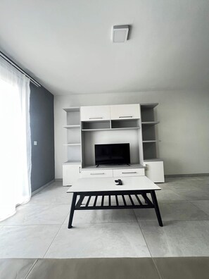 A modern living room with a flat-screen TV, white cabinetry, and a coffee table. - Swieqi Spacious 3 BDR Apartment by PMI Malta (Is-Swieqi)