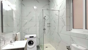 Un bagno moderno con box doccia in vetro, lavatrice a incasso, un water e un lavandino con mobile contenitore in legno scuro.