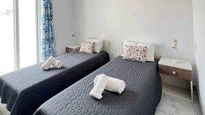 Camera d'albergo con due letti, una finestra con tende, un comodino con una lampada e una lampada a sospensione.