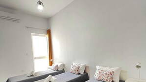 Una camera d'albergo con due letti, un comodino, una lampada e una finestra con tende.