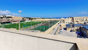 Un estadio con varias canchas deportivas, un área de estacionamiento y edificios al fondo.