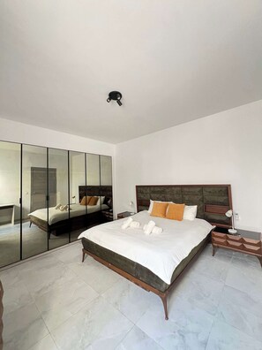 Ein Schlafzimmer mit einem großen Bett, einem Nachttisch, einem Spiegel und einer Deckenleuchte.