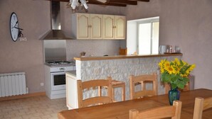 Una cocina con encimera de piedra, sillas de madera, una mesa de comedor, un reloj y una ventana.
