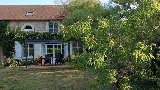 Ein Haus mit überdachter Terrasse, umzäunter Garten und einem Baum.