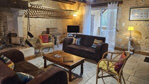 Ein rustikales Wohnzimmer mit freiliegenden Holzbalken, einer Steinwand, einem Kamin, einem Fernseher und Korbmöbeln.