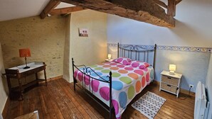 Ein Schlafzimmer mit Holzboden, einem Bett mit Punkten, einem Nachttisch, einer Lampe, einem kleinen Tisch ebenfalls mit Lampe und einem Heizkörper.