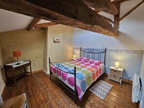 A bedroom with a wooden floor, a bed with a polka dot bedspread, a nightstand, a lamp, a small table with a lamp, and a radiator. - Les Hirondelles - LUSIGNAN (LUSIGNAN)