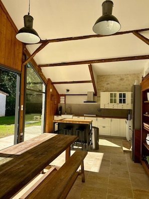 A rustic kitchen with wooden beams, a wooden table, and a view of the outdoors. - Clos de La Brelaisiere (CHAUVIGNY)
