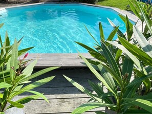 A swimming pool with clear blue water, surrounded by wooden decking and green foliage. - Clos de La Brelaisiere (CHAUVIGNY)
