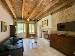 A living room with a fireplace, stone wall, wooden ceiling beams, and a flat-screen TV. - Clos de La Brelaisiere (CHAUVIGNY)